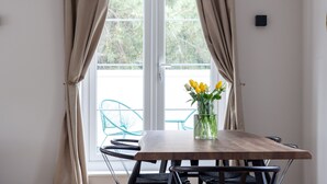 A dining area with a wooden table, chairs, a vase with flowers, and a view through a window with curtains.