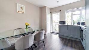 Une cuisine moderne avec une table à manger en verre, des chaises grises et une vue sur l’extérieur.
