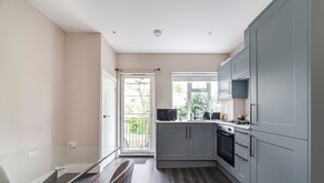 Une cuisine moderne avec des meubles de couleur grise, un four encastré et une fenêtre donnant sur un balcon.
