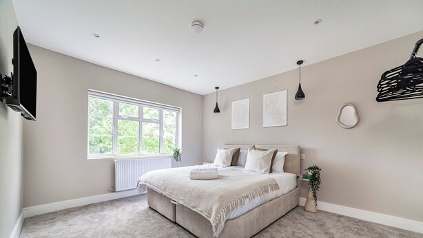 Une chambre à coucher avec un lit, une fenêtre, un radiateur, une lampe suspendue et un téléviseur fixé au mur.
