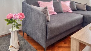 A grey sofa with pink cushions, a white vase with pink flowers, and a wooden side table. - Gorgeous apartment in Pula with WiFi (Pula)