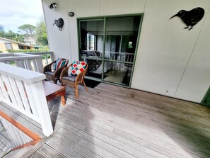 A wooden deck with two wicker chairs and a table, a sliding glass door, and a wall-mounted bird sculpture.