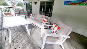 A covered outdoor seating area with white furniture, including a table and two sofas, on a wooden deck.