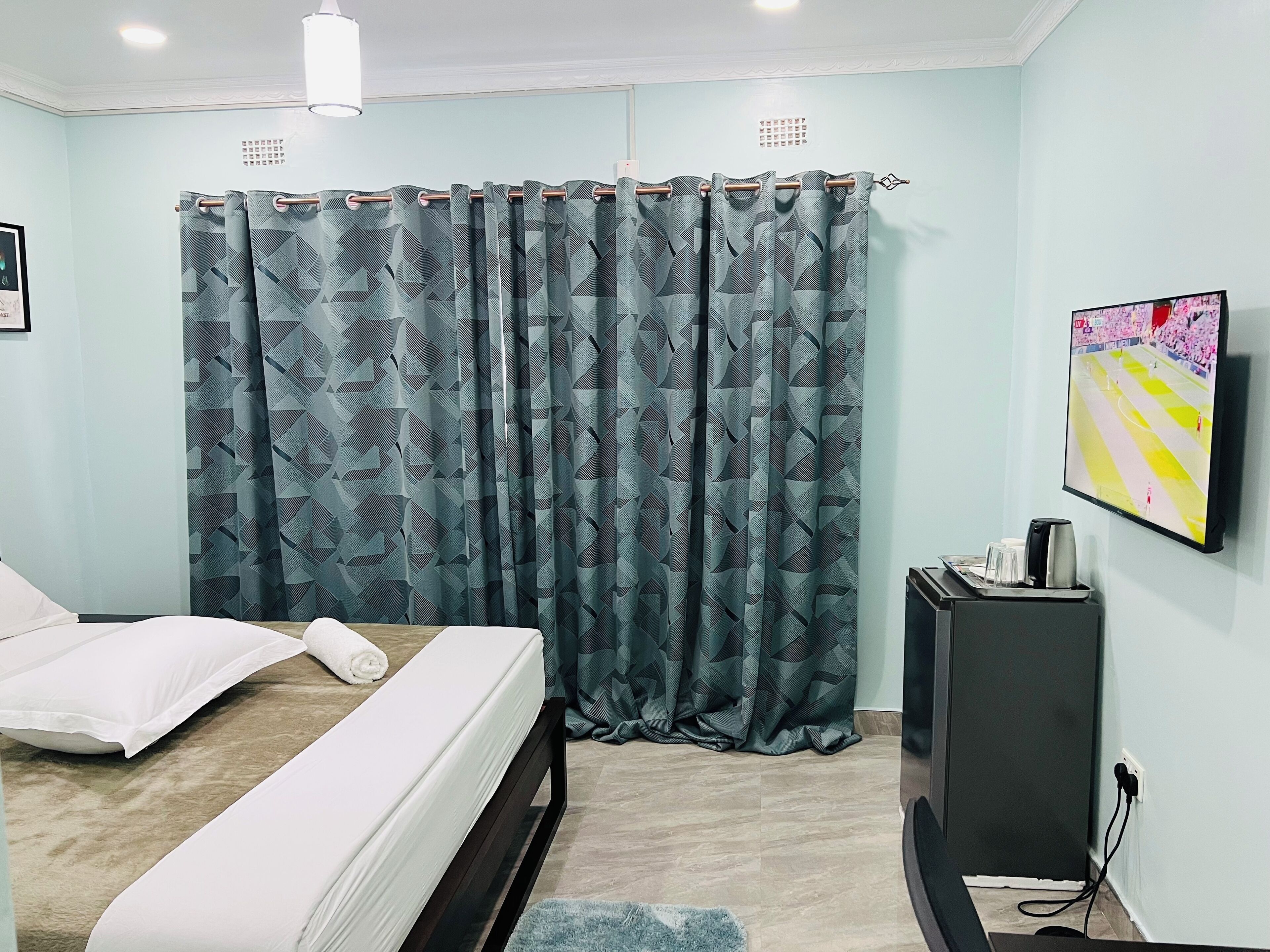 A bedroom with a bed, a TV, and a curtain with a geometric pattern.
