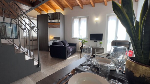 A modern living room with a sofa, a dining table set with plates and glasses, a staircase with metal railings, and a television on the wall. - Medieval IV - Historic Experience in Como (Como)
