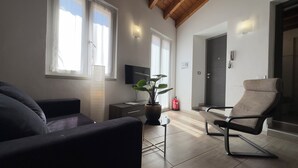 A living room with a sofa, a chair, a potted plant, a television, and a door leading to another room. - Medieval IV - Historic Experience in Como (Como)
