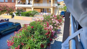 Ein zweistöckiges Gebäude mit Balkon, einem geparkten Auto davor und blühenden Pflanzen entlang des Gehwegs.