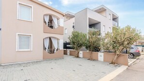 Ein modernes Apartmenthaus mit Balkonen, einer gepflasterten Auffahrt und Blumentöpfen.