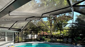 Una piscina exterior cubierta con techo metálico, rodeada de sillas y plantas en macetas.