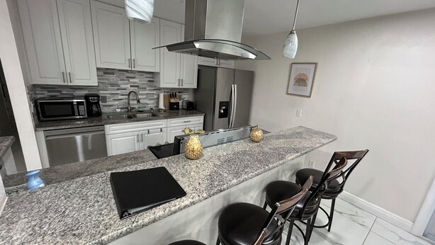 Una cocina moderna con encimeras de granito, electrodomésticos de acero inoxidable y taburetes de bar.