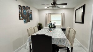 Un comedor con una mesa, sillas, ventilador de techo y ventana con cortinas.
