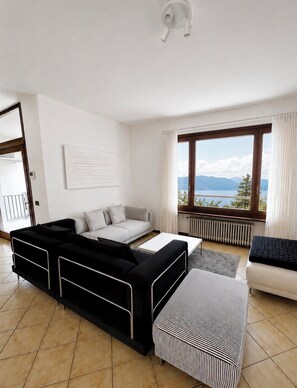 A modern living room with a sofa, a coffee table, and a view of the outdoors. - Cà Sulà, a large single-family home with a garden and a beautiful view of the lake (Maccagno con Pino e Veddasca)