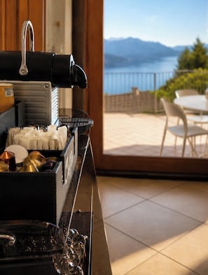 A kitchen with a coffee machine, tea pots, and a view of a balcony with outdoor furniture. - Cà Sulà, large detached house with garden and beautiful lake view (Maccagno con Pino e Veddasca)