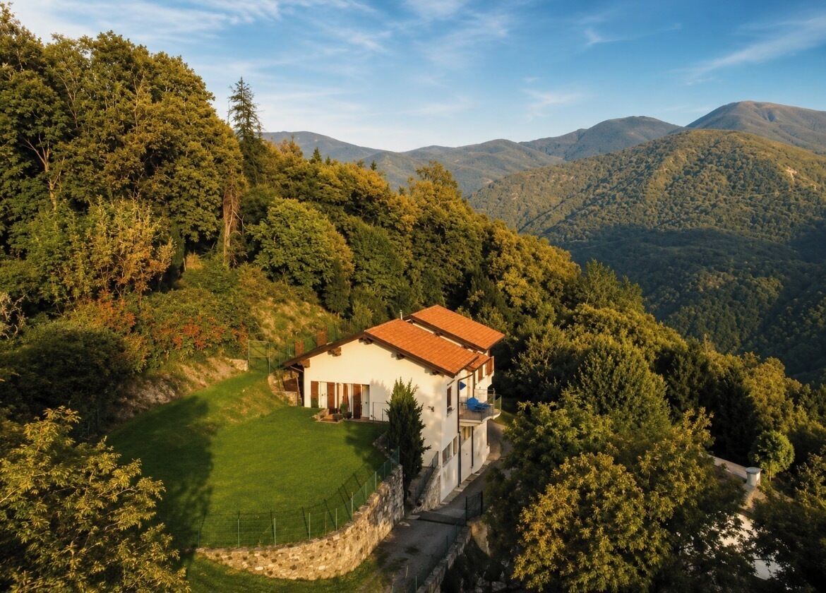 Ein eingeschossiges Haus mit rotem Ziegeldach, umgeben von üppiger Vegetation und sanften Hügeln im Hintergrund.
