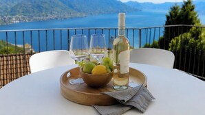 A table with a bottle of white wine, glasses, and a bowl of fruit on a wooden tray, overlooking a mountainous landscape. - Cà Sulà, large detached house with garden and beautiful lake view (Maccagno con Pino e Veddasca)