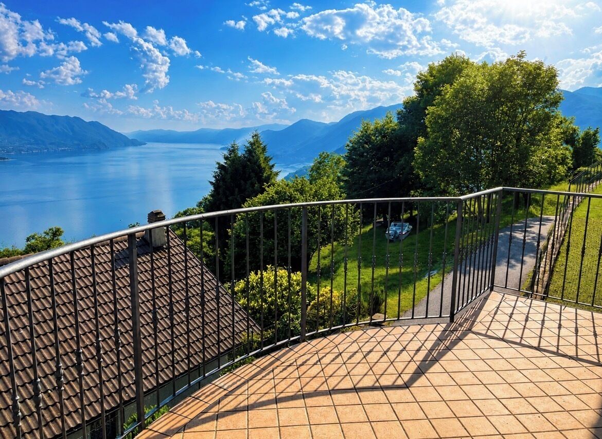 A balcony with a metal railing overlooking a lake and mountains.