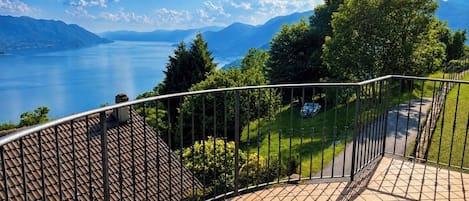 A balcony with a metal railing overlooking a lake and mountains.