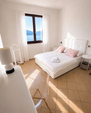 A bedroom with a bed, a desk, a chair, a nightstand, and a window with a view of the sea. - Cà Sulà, large detached house with garden and beautiful lake view (Maccagno con Pino e Veddasca)