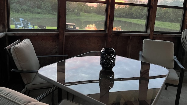 A room with a glass table, two chairs, and a view of a sunset over a lake.
