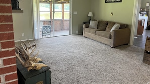 A living room with a sofa, a coffee table with antlers, a sliding glass door leading to a patio, and a kitchen in the background.