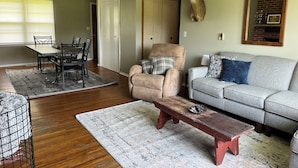 A living room with a dining table, a sofa, a chair, and a deer head mounted on the wall.
