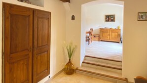 A hallway with wooden doors, a vase with plants, and a dining area with a table and chairs. - 06CB : Pretty country house for 8 (Tourrettes-sur-Loup)