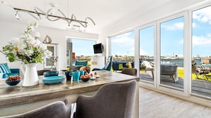 Un espace repas moderne, doté d’une grande table, de chaises et offrant une vue sur la mer.