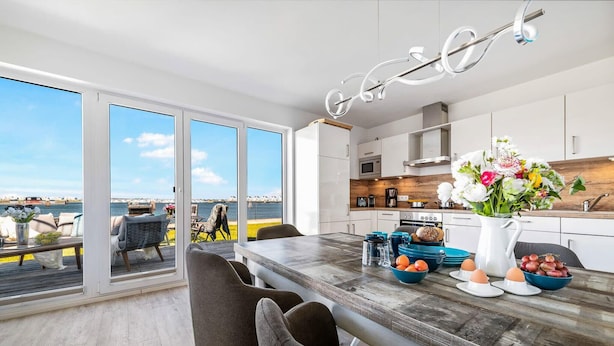 Une cuisine moderne avec vue sur la mer, dotée d’un plan de travail en bois, de meubles blancs et d’un luminaire suspendu.