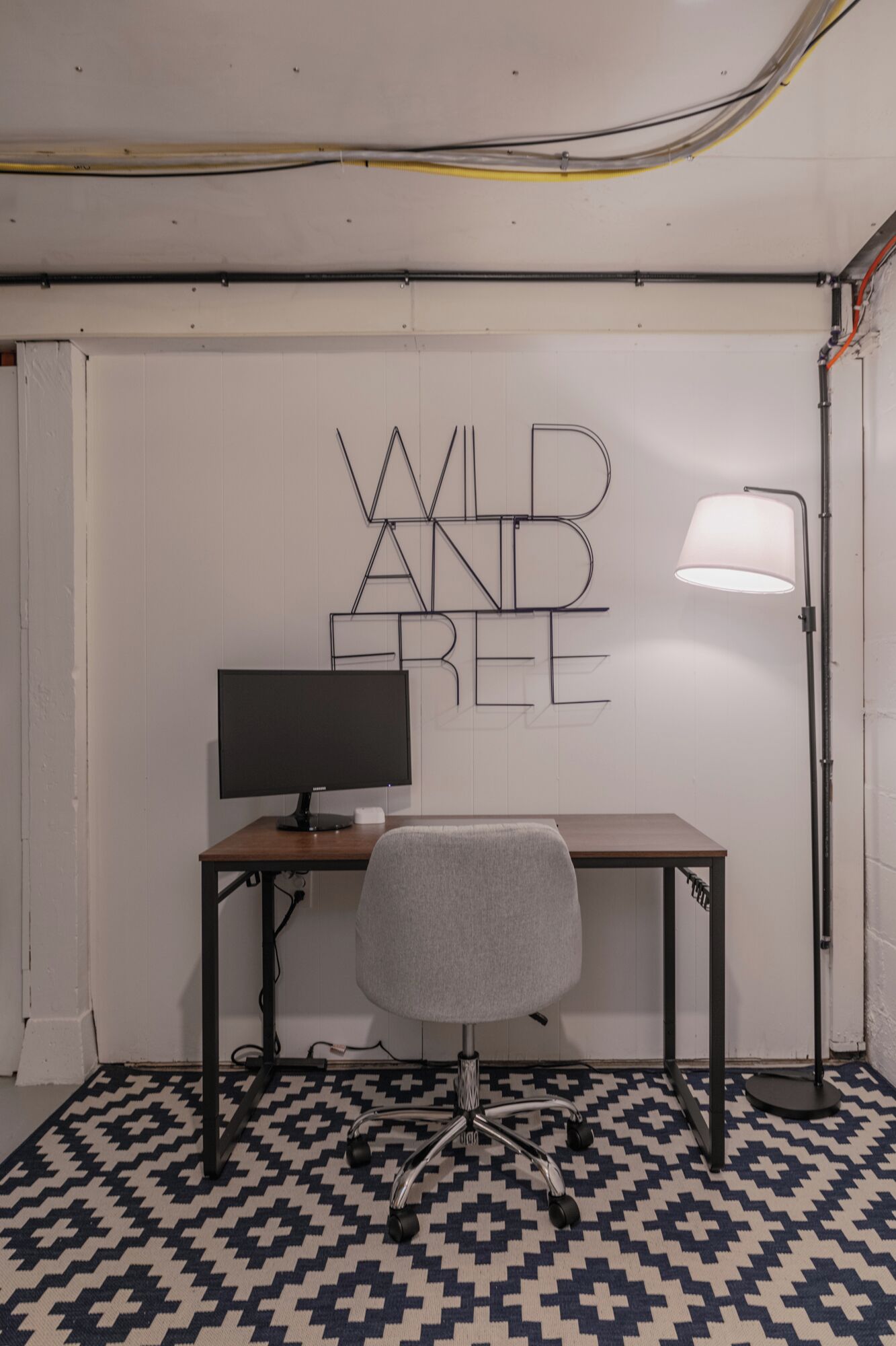 Una stanza con una scrivania, una sedia e una parete decorata con la scritta ‘WILD AND FREE’ in un design geometrico.