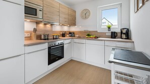 Een moderne keuken met witte kastjes, een inbouwoven, een magnetron en een koffiezetapparaat.