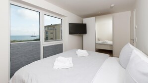 Una habitación de hotel con una cama grande, un televisor de pantalla plana en la pared y vistas al mar a través de las ventanas.