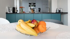 Una mesa de comedor con un frutero que contiene plátanos, una manzana y una naranja.
