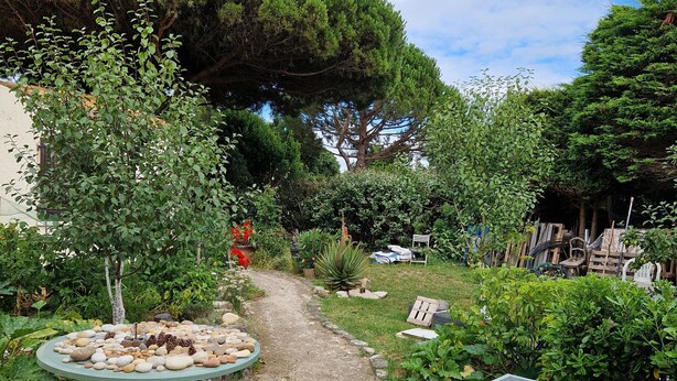 Un jardin avec une table et des chaises, un chemin de pierres et diverses plantes.