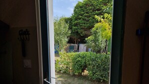 Une porte qui donne sur un jardin où l’on trouve une grande variété de plantes et un arbre.