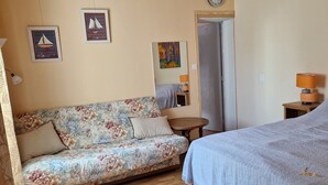 Une pièce chaleureuse avec un plafond en bois, un canapé à motifs floraux, un lit recouvert d’une couverture bleue et une petite table en bois.