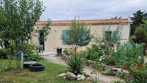 Un jardin avec un sentier menant à un bâtiment doté d’un toit en tuiles. On y trouve différentes plantes et une petite table.