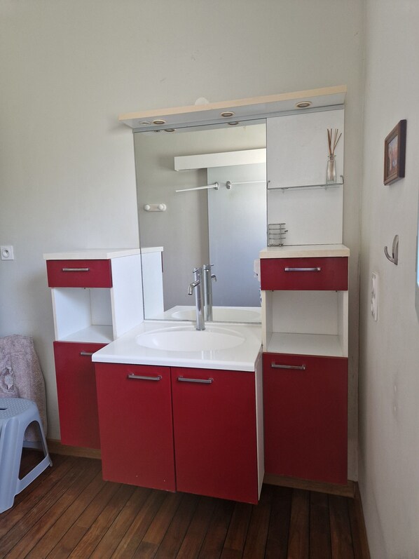 Un baño con lavamanos blanco, armarios rojos y espejo sobre el lavamanos.