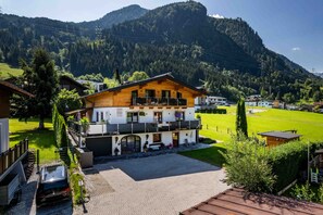 A two-story wooden chalet with a balcony, surrounded by a well-maintained lawn and a mountain backdrop. - Haus Katharina - Kitzsteinhornblick (Kaprun)