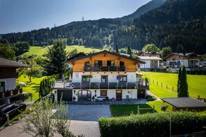 A two-story chalet with a balcony, surrounded by a well-maintained lawn and a mountain backdrop.