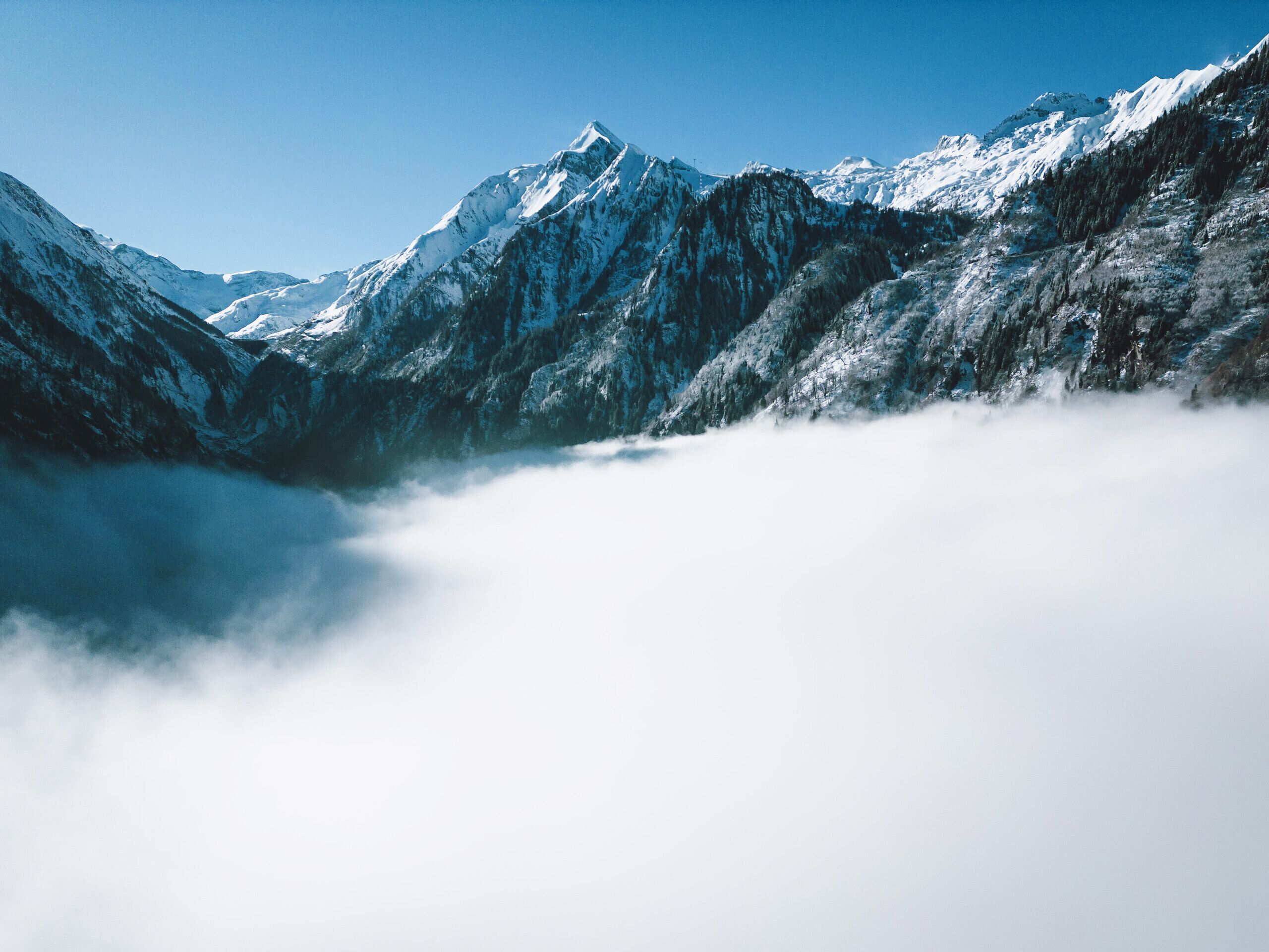 Eine Berglandschaft mit schneebedeckten Gipfeln und einem nebelverhangenen Tal.