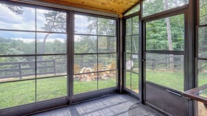 Una habitación con ventanas amplias, techo de madera y vistas a un espacio exterior con sillas y una valla.