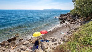 A rocky beach with clear blue water, a person sunbathing, and colorful umbrellas. - 1 bedroom lovely apartment in Ika (Ika)