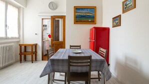 Un comedor con una mesa dispuesta para dos personas, un refrigerador rojo y un cuadro en la pared.