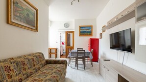 Una sala de estar con un sofá, una mesa de comedor con sillas, un armario rojo y un televisor montado en la pared.