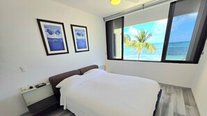 A bedroom with a bed, a nightstand, a window with a view of the ocean, and two framed pictures on the wall. - Oceanfront Condo at Unique Location (Cancun)