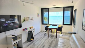 A modern living room with a large TV, a dining area, and a view of the sea. - Oceanfront Condo at Unique Location (Cancun)
