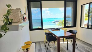 A dining area with a view of the sea, a wooden table, yellow chairs, and colorful bowls on the floor. - Oceanfront Condo at Unique Location (Cancun)