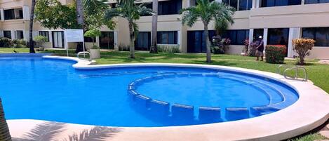A swimming pool with a circular design, surrounded by a well-maintained lawn and palm trees.