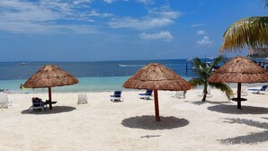A beach with thatched umbrellas, white lounge chairs, and a clear view of the ocean. - Oceanfront Condo at Unique Location (Cancun)