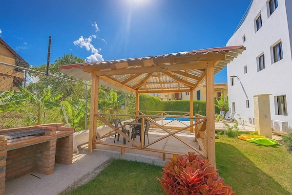 Une structure de pergola en bois, avec une piscine en arrière-plan.